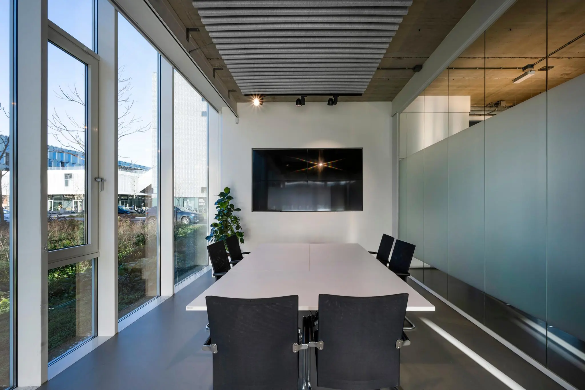 Moderne vergaderruimte aan de Fred. Roeskestraat met glazen wanden, grote ramen en een scherm aan de muur.